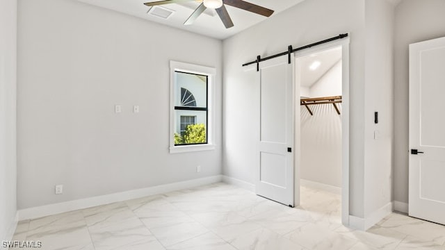 unfurnished bedroom with ceiling fan, a barn door, a spacious closet, and a closet