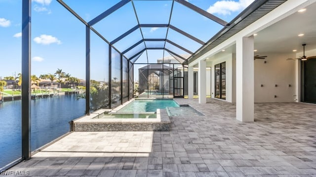 view of swimming pool featuring glass enclosure, ceiling fan, a patio area, an in ground hot tub, and a water view