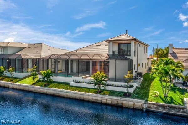 back of property with a balcony, a water view, a lanai, and a lawn