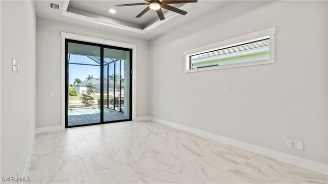 empty room with ceiling fan and a tray ceiling