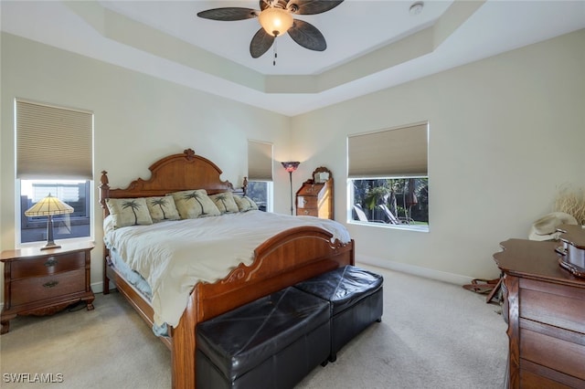 bedroom with baseboards, a raised ceiling, a ceiling fan, and light colored carpet