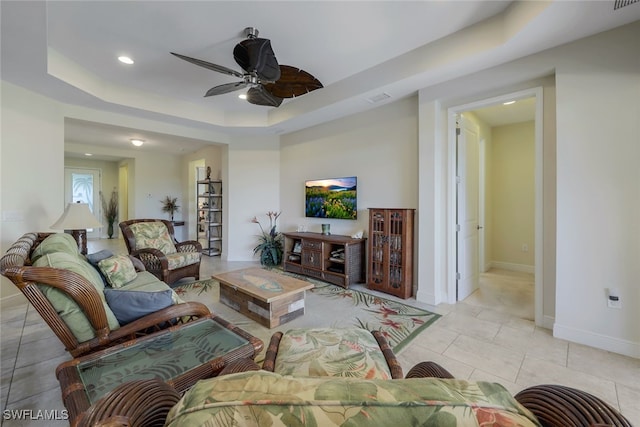 living room with light tile patterned floors, visible vents, baseboards, a ceiling fan, and a tray ceiling