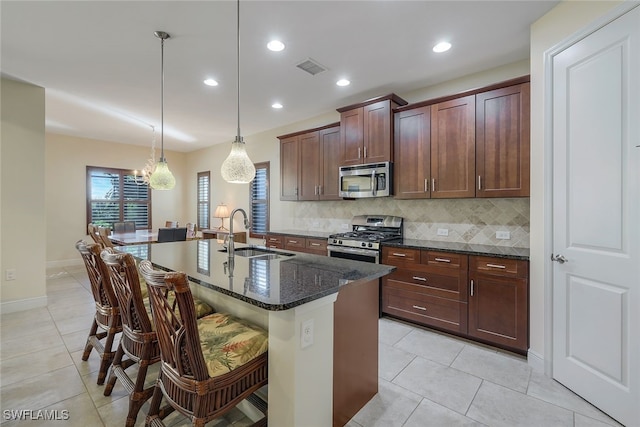 kitchen featuring a breakfast bar area, hanging light fixtures, a kitchen island with sink, stainless steel appliances, and a sink