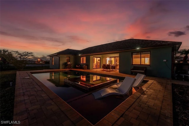 pool at dusk featuring a jacuzzi and a patio area