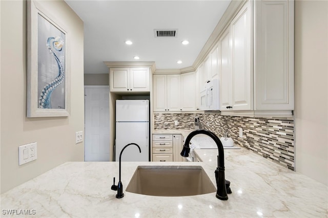 kitchen featuring light stone countertops, sink, white cabinetry, tasteful backsplash, and white appliances