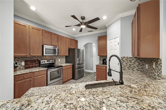 kitchen with appliances with stainless steel finishes, light wood-type flooring, tasteful backsplash, ornamental molding, and sink