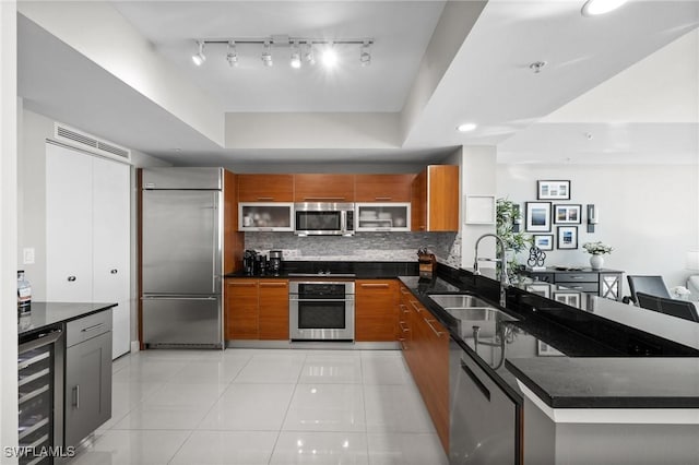 kitchen featuring sink, decorative backsplash, dark stone countertops, appliances with stainless steel finishes, and beverage cooler