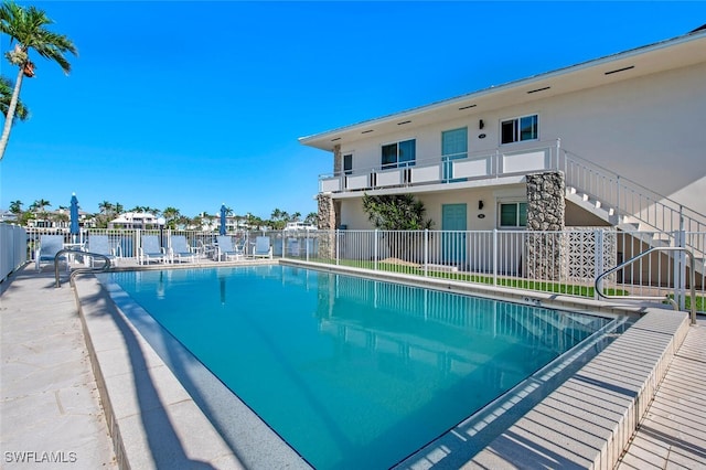 pool with a water view, stairs, fence, and a patio