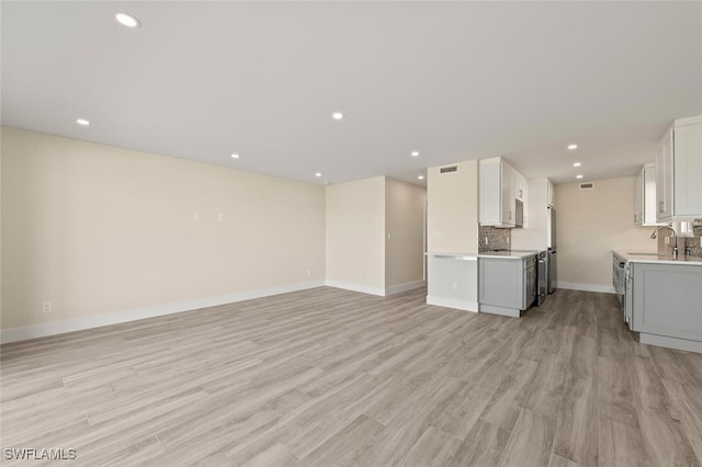 kitchen featuring a sink, white cabinets, open floor plan, light countertops, and tasteful backsplash