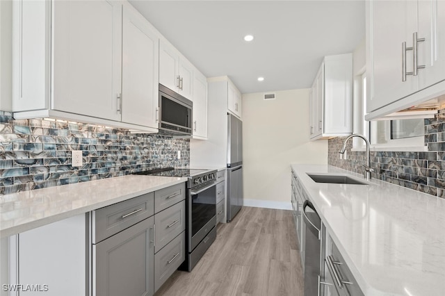 kitchen featuring light stone counters, appliances with stainless steel finishes, a sink, and white cabinetry