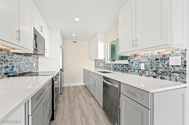 kitchen featuring light wood finished floors, stainless steel appliances, white cabinetry, a sink, and light stone countertops