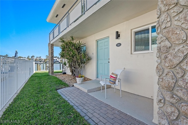 view of exterior entry featuring a yard, a patio area, fence, and stucco siding