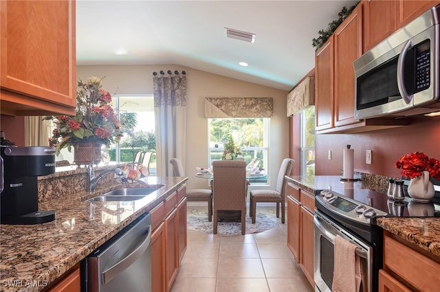 kitchen with light stone counters, light tile patterned floors, lofted ceiling, appliances with stainless steel finishes, and sink