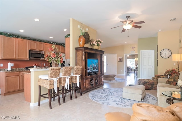 kitchen with a kitchen breakfast bar, appliances with stainless steel finishes, light tile patterned floors, ceiling fan, and lofted ceiling