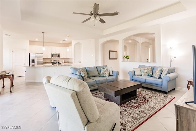 tiled living room with a raised ceiling and ceiling fan