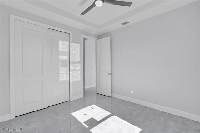 unfurnished bedroom with a tray ceiling, ceiling fan, and a closet