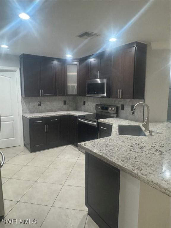 kitchen with decorative backsplash, light stone counters, stainless steel appliances, sink, and light tile patterned flooring