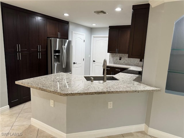 kitchen featuring dark brown cabinetry, light stone countertops, sink, kitchen peninsula, and stainless steel fridge