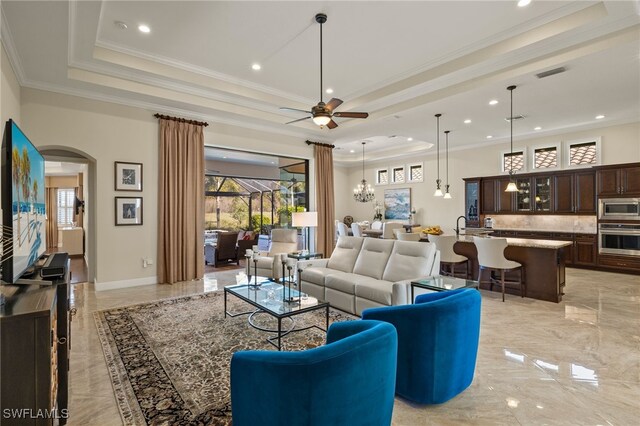 living room with ceiling fan with notable chandelier, ornamental molding, and a tray ceiling