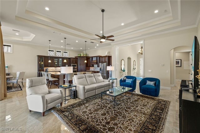 living room with a raised ceiling, ceiling fan, and ornamental molding