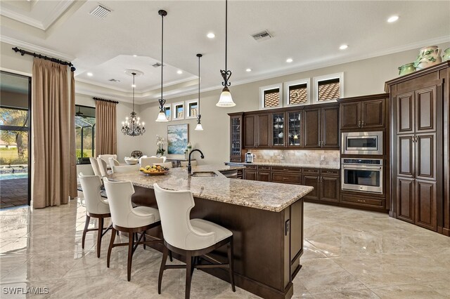 kitchen featuring hanging light fixtures, stainless steel appliances, a kitchen breakfast bar, backsplash, and a large island with sink