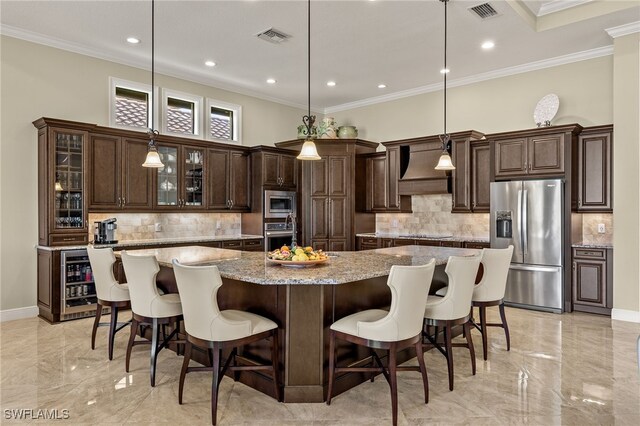 kitchen featuring light stone countertops, appliances with stainless steel finishes, custom range hood, a large island with sink, and pendant lighting