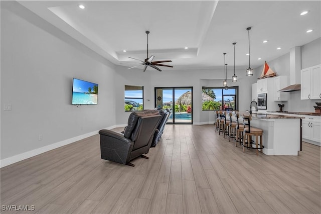 living room featuring sink, a raised ceiling, ceiling fan, and light hardwood / wood-style floors