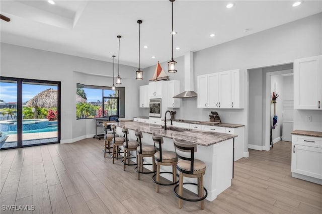 kitchen with sink, white cabinets, a kitchen island with sink, dark stone counters, and pendant lighting