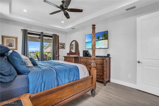 bedroom with ceiling fan, a tray ceiling, access to exterior, and light hardwood / wood-style flooring