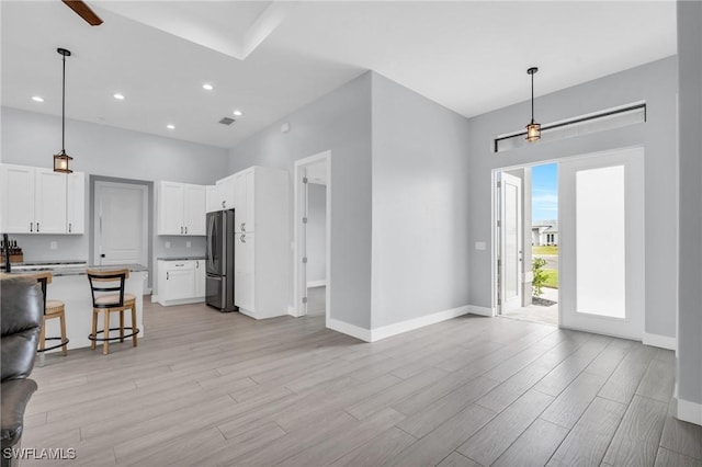 kitchen with a kitchen bar, decorative light fixtures, white cabinetry, and stainless steel refrigerator