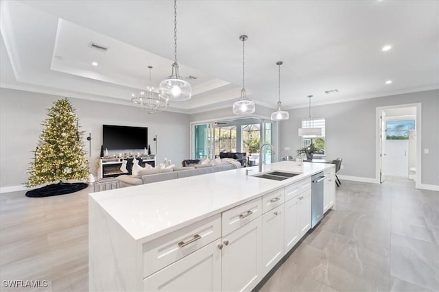 kitchen featuring sink, white cabinetry, a tray ceiling, hanging light fixtures, and a kitchen island with sink