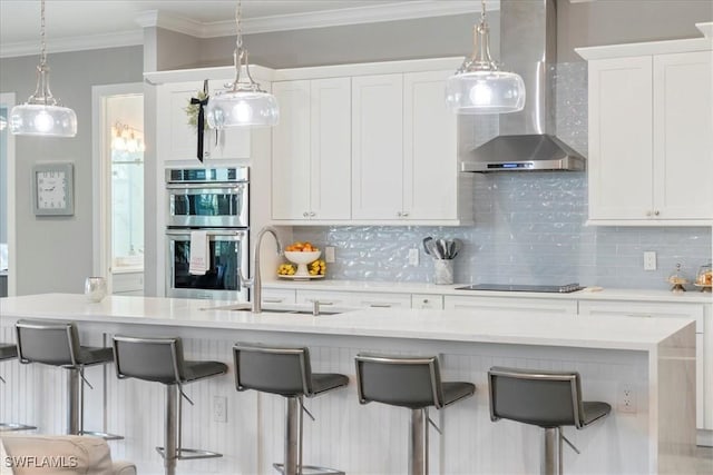 kitchen with wall chimney range hood, white cabinets, and stainless steel double oven