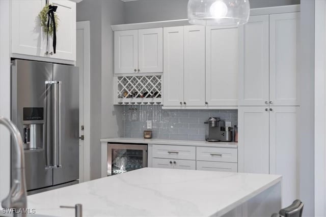 kitchen with pendant lighting, wine cooler, high quality fridge, white cabinets, and decorative backsplash