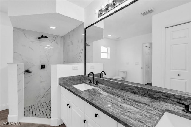 bathroom with wood-type flooring, a tile shower, vanity, and toilet