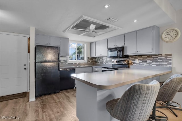 kitchen featuring black appliances, light wood-type flooring, kitchen peninsula, and a breakfast bar area