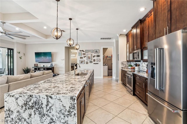 kitchen with appliances with stainless steel finishes, light stone counters, a spacious island, sink, and pendant lighting