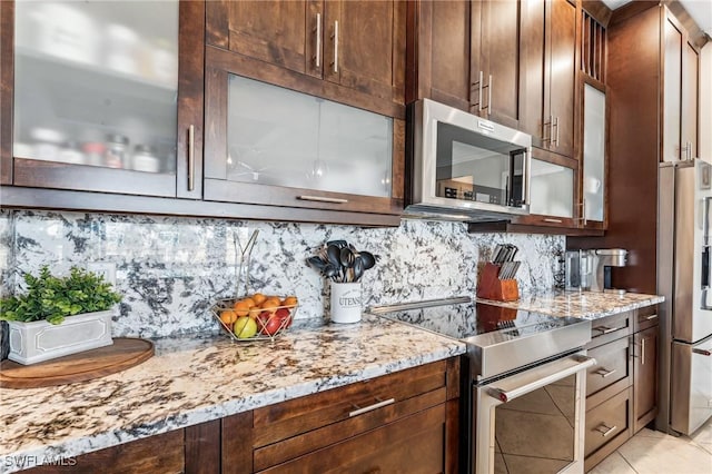 kitchen with backsplash, light stone counters, light tile patterned flooring, and stainless steel appliances