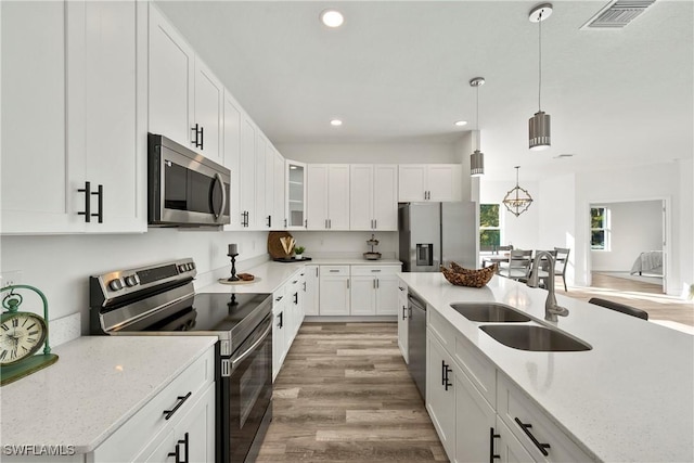 kitchen featuring light stone countertops, white cabinetry, sink, appliances with stainless steel finishes, and light wood-type flooring