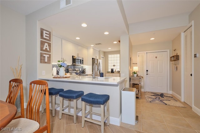 kitchen featuring kitchen peninsula, white cabinetry, stainless steel appliances, and decorative backsplash