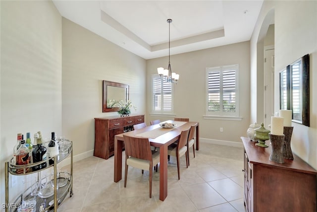 dining area featuring a raised ceiling, light tile patterned floors, a healthy amount of sunlight, and an inviting chandelier