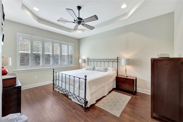 bedroom with ceiling fan, dark hardwood / wood-style floors, and a raised ceiling