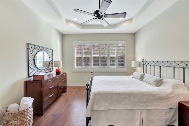 bedroom featuring ceiling fan, dark hardwood / wood-style floors, multiple windows, and a tray ceiling