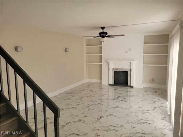 unfurnished living room with built in shelves, ceiling fan, and a high end fireplace