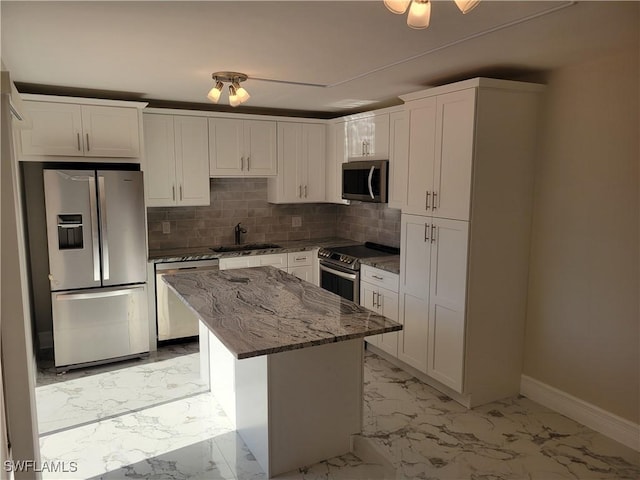 kitchen with light stone counters, stainless steel appliances, sink, white cabinets, and a center island