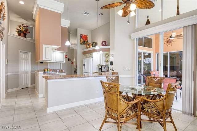 kitchen with ceiling fan, white fridge with ice dispenser, kitchen peninsula, a towering ceiling, and light tile patterned floors