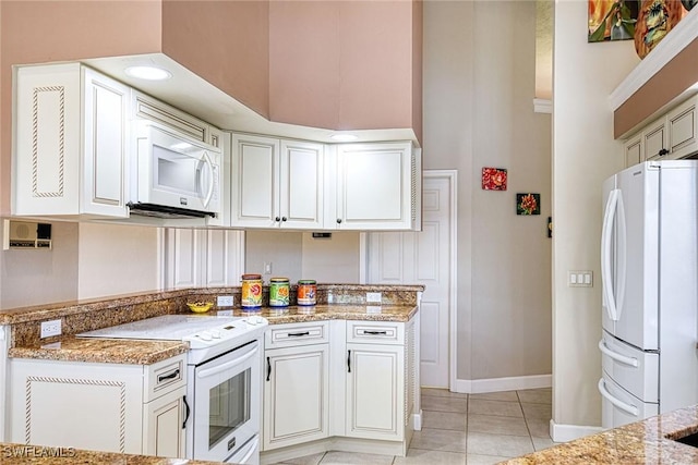 kitchen featuring a towering ceiling, light stone counters, white appliances, light tile patterned floors, and white cabinetry