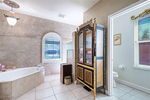 bathroom featuring tile patterned flooring, a relaxing tiled tub, toilet, and a healthy amount of sunlight