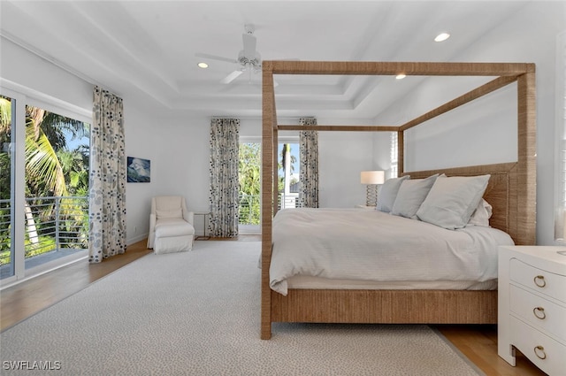 bedroom with a raised ceiling, ceiling fan, light hardwood / wood-style flooring, and access to outside