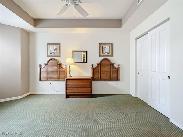 unfurnished bedroom with dark colored carpet, ceiling fan, a tray ceiling, and a closet