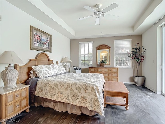 bedroom with ceiling fan, dark hardwood / wood-style floors, and a tray ceiling